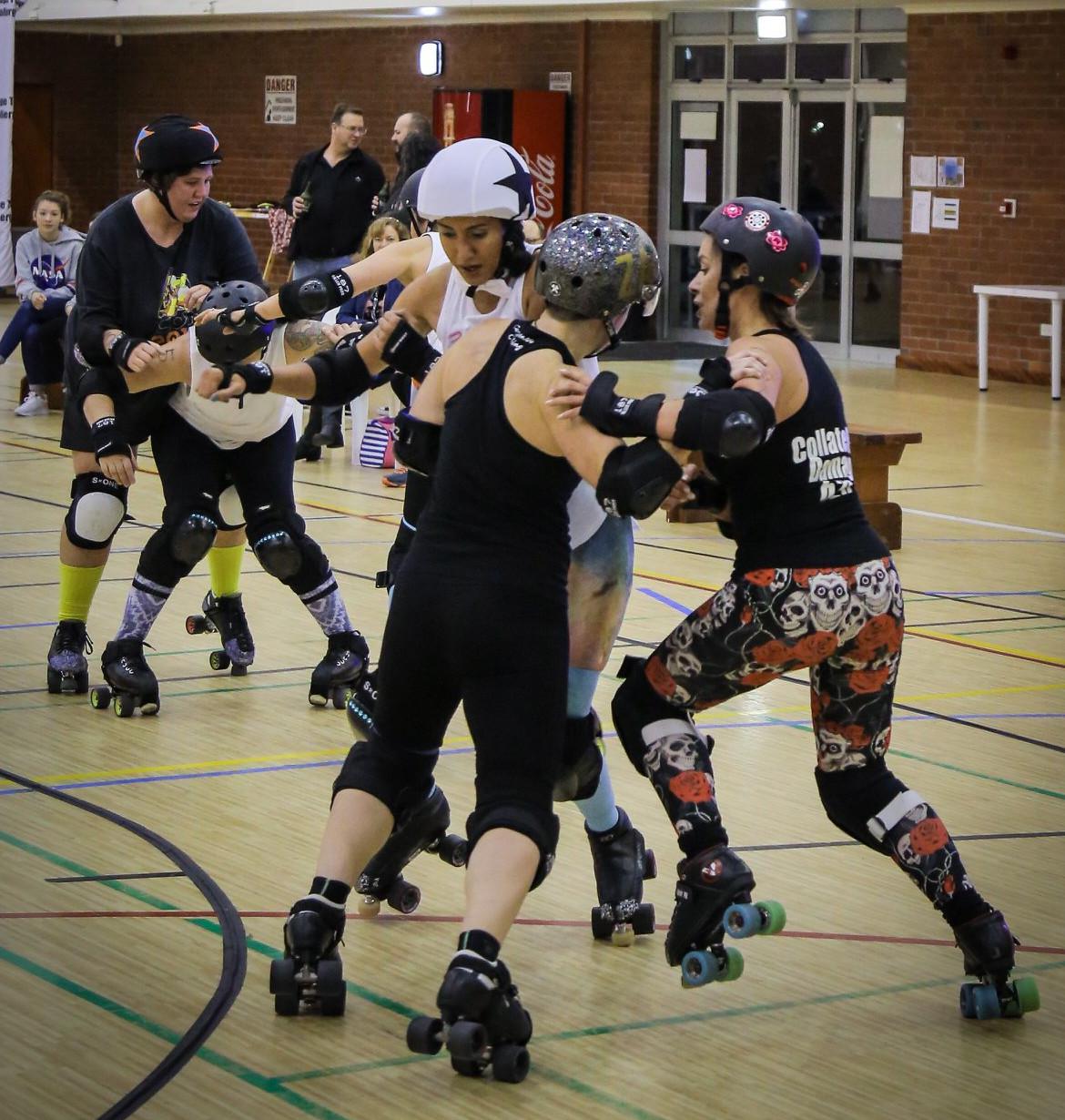 Action shot of Cape Town Rollergirls' third Short Track bout; pack in two halves, white jammer held at front by blockers, black jammer held at back.